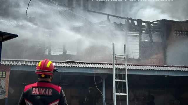 Petugas damkar memanjat atap kios untuk menjangkau sumber api di Pasar Kuliner Malinau.