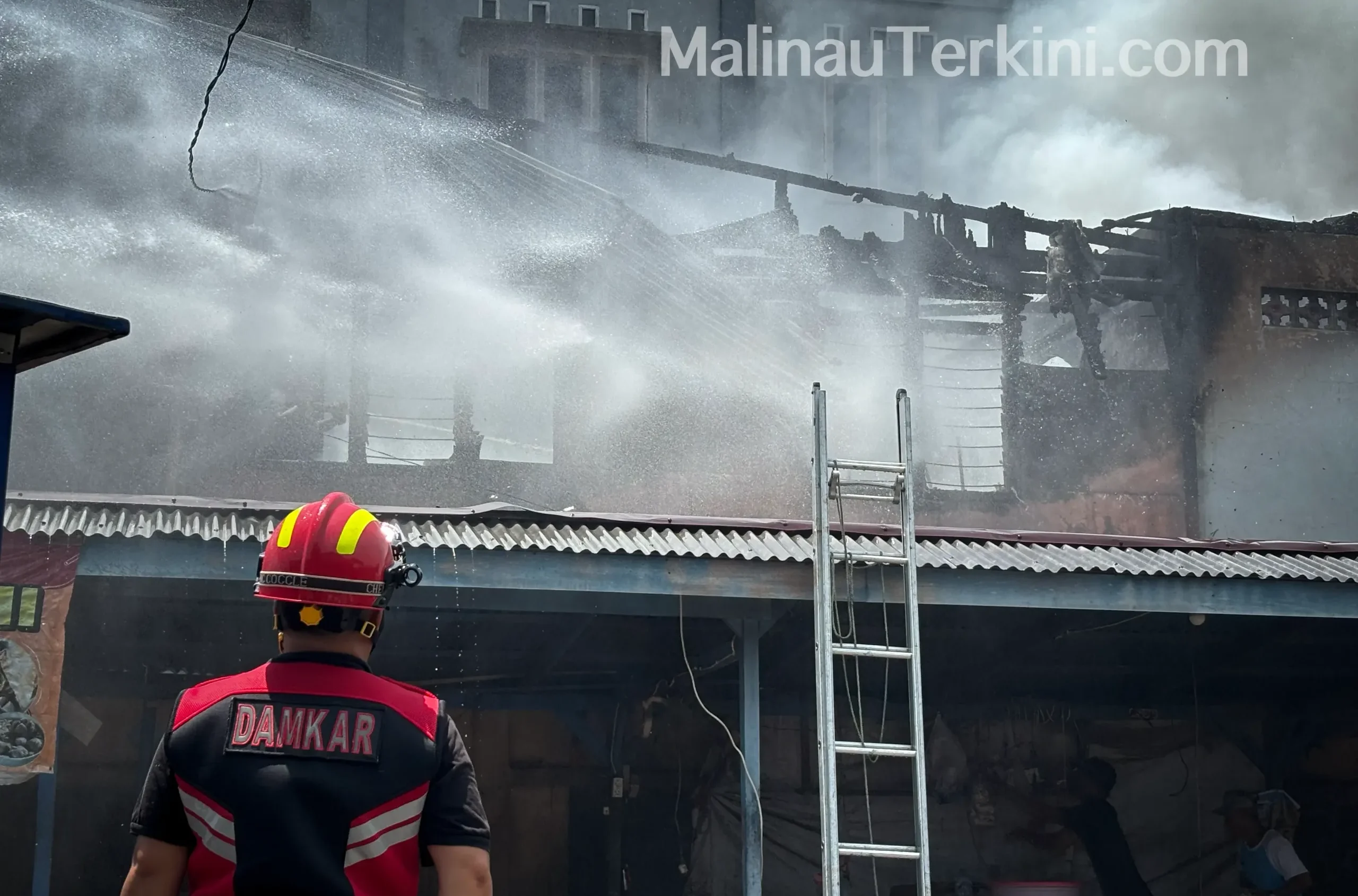 Petugas damkar memanjat atap kios untuk menjangkau sumber api di Pasar Kuliner Malinau.
