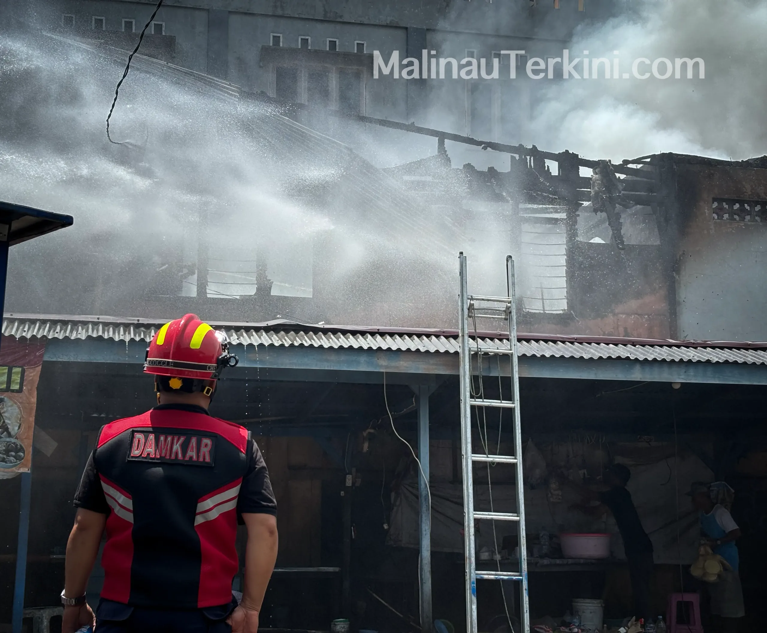 Petugas damkar memanjat atap kios untuk menjangkau sumber api di Pasar Kuliner Malinau.