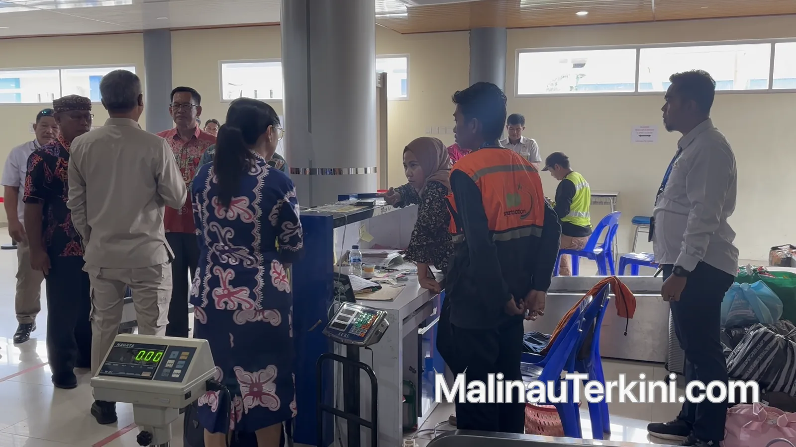 Suasana di area lapor diri (check-in) Bandara Malinau yang memperlihatkan penumpang sedang berinteraksi dengan petugas di depan meja pelayanan.