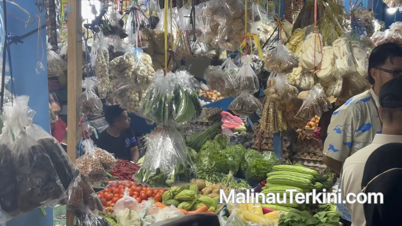 Seorang pedagang pria sedang menyusun telur ayam di dalam rak kayu dan wadah keranjang di sebuah kios pasar.