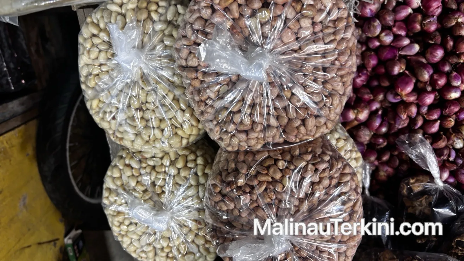 Tumpukan kacang tanah mentah di atas meja dagangan pasar tradisional dengan latar belakang aktivitas warga.