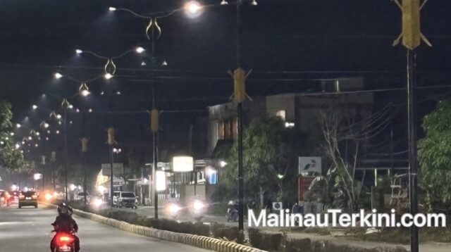 Pemandangan malam hari jalan raya di Malinau yang diterangi lampu jalan dekoratif yang cerah, memperlihatkan kendaraan bermotor melintas di bawah cahaya lampu.