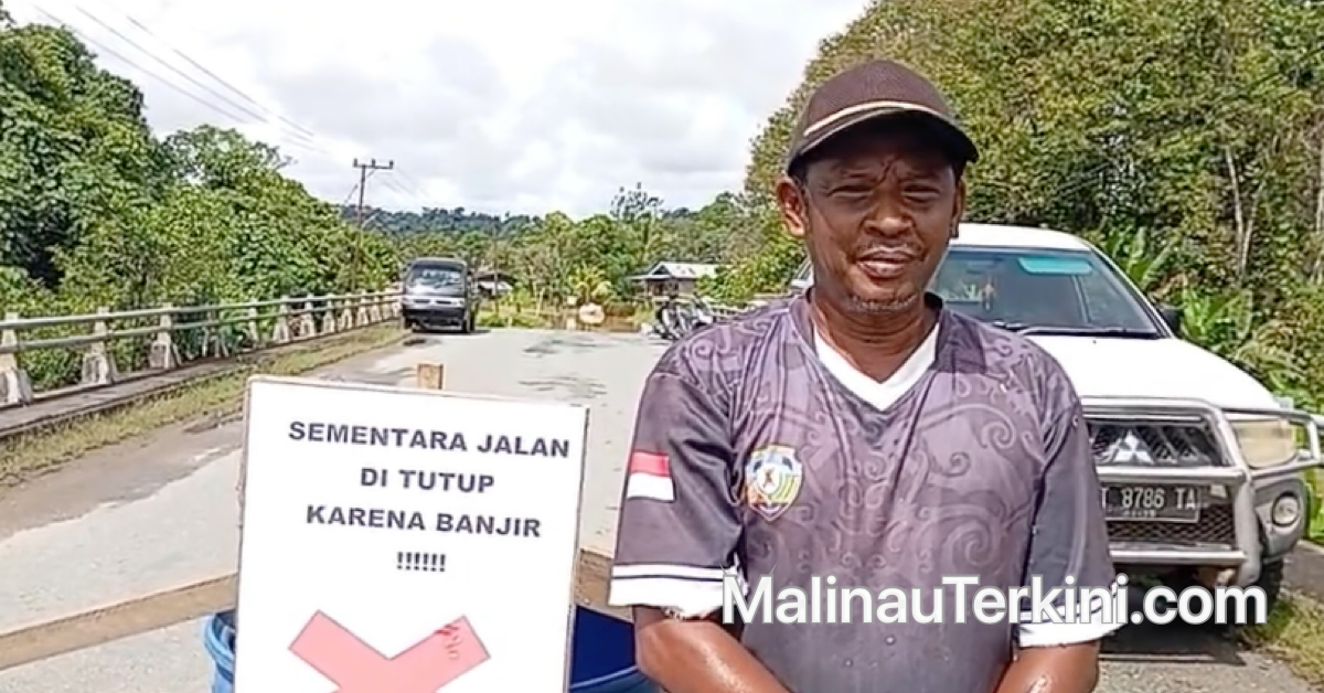 potret Berahim, Ketua RT 14 Desa Tanjung Lapang, yang mengenakan kaus dan topi, berdiri di area terbuka dekat lokasi terdampak banjir.